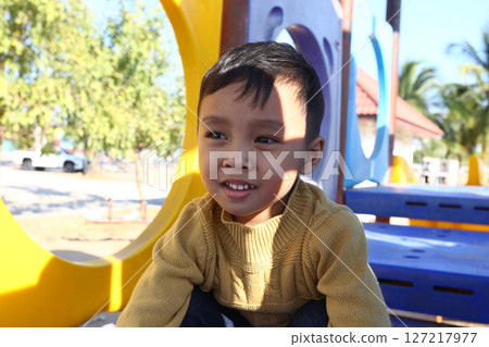 Happy child enjoying outdoor playground activities on a sunny day, wearing a cozy sweater, surrounded by colorful play structures in a joyful environment Happy child enjoying outdoor playground activities on a sunny day, wearing a cozy sweater, surrounded by colorful play structures in a joyful environment 127217977