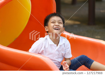 Joyful Young Boy Having Fun on Colorful Slide in Playground, Enjoying Outdoor Activity with Bright Smile and Clear Happiness During Sunny Day 127217988