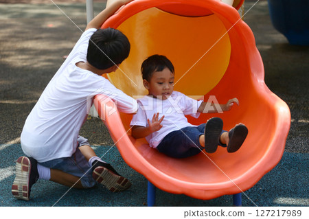 Two Young Boys Playing Together on a Colorful Playground Slide, Engaging in Fun and Playful Activities Outdoors at a Sunny Day in a Park Environment 127217989