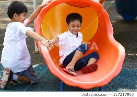 Two Children Playing Joyfully on a Colorful Slide in a Playground, Capturing the Essence of Childhood Fun and Friendship in Outdoor Playtime Activities 127217990