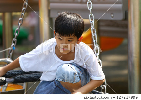 Young boy playing on a swing in a vibrant playground setting, showcasing joy and carefree childhood moments in a sunny outdoor environment. 127217999