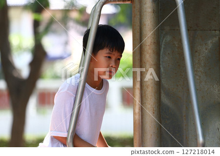 Young Boy Engaged in Outdoor Play on a Sunny Day, Climbing Playground Equipment in a Park Setting With Focused Expression and Natural Backdrop 127218014