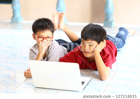 Two Asian Boys Engaged with Laptop on Floor in Bright Room, One in Glasses, Explore Online Learning and Playful Interaction, Casual Indoor Environment 127218033