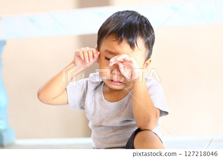 Emotional Young Child with Tearful Expression Sitting on Floor, Experiencing Sadness, Vulnerability, and Innocence in Natural Indoor Light Setting 127218046