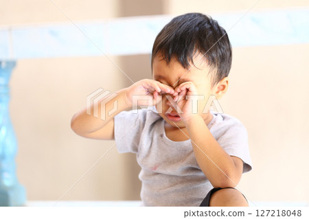 Upset Young Boy Sitting on Floor with Hands Covering Face, Expressing Sadness or Distress in Indoor Setting with Natural Light and Soft Background 127218048