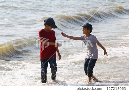 Two Young Boys Playing on a Sandy Beach, Enjoying a Sunny Day Together, Making Memories at the Shoreline with Gentle Waves and Warm Embrace of Nature 127218063