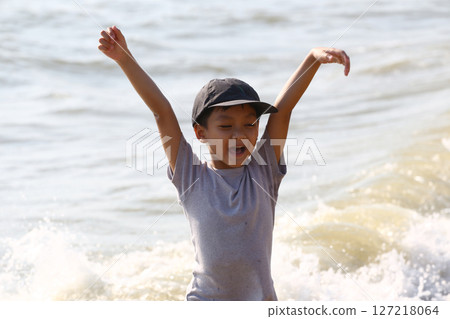 Joyful Child Playing in Shallow Water at the Beach with Hands Raised, Enjoying Nature and Summer Vibes on a Sunny Day by the Shoreline Joyful Child Playing in Shallow Water at the Beach with Hands Raised, Enjoying Nature and Summer Vibes on a Sunny Day by the Shoreline 127218064