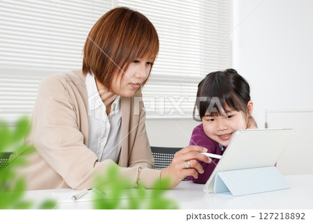 A woman helping a child learn using a tablet and an elementary school student learning from her A woman helping a child learn using a tablet and an elementary school student learning from her 127218892