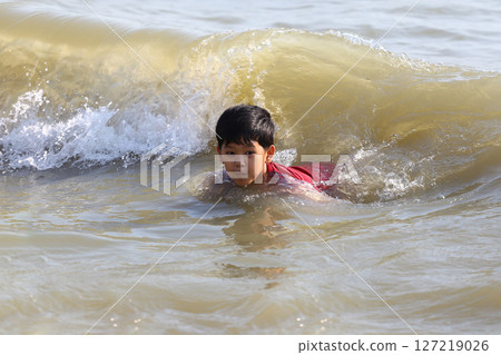 Young boy enjoying the waves while swimming in the ocean, showcasing a moment of joy and adventure in a sunny beach environment with gentle surf and warm sunlight. Young boy enjoying the waves while swimming in the ocean, showcasing a moment of joy and adventure in a sunny beach environment with gentle surf and warm sunlight. 127219026