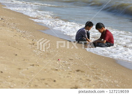 Two Young Boys Playing in Shallow Water on Sandy Beach, Enjoying a Summer Day, Building Sandcastles, and Creating Lasting Memories by the Ocean Shore Two Young Boys Playing in Shallow Water on Sandy Beach, Enjoying a Summer Day, Building Sandcastles, and Creating Lasting Memories by the Ocean Shore 127219039