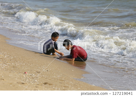 Two Young Boys Playing at the Shoreline, Enjoying the Waves and Sand on a Sunny Day, Capturing the Joy and Bonding Moments of Childhood by the Ocean Two Young Boys Playing at the Shoreline, Enjoying the Waves and Sand on a Sunny Day, Capturing the Joy and Bonding Moments of Childhood by the Ocean 127219041