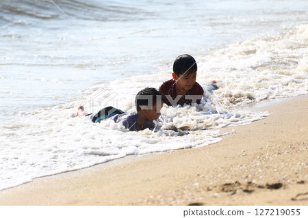 Two Young Boys Playing in Shallow Sandy Water at the Beach, Enjoying Splashes and Waves under a Bright Sunny Sky, Capturing Pure Joy and Childhood Fun 127219055