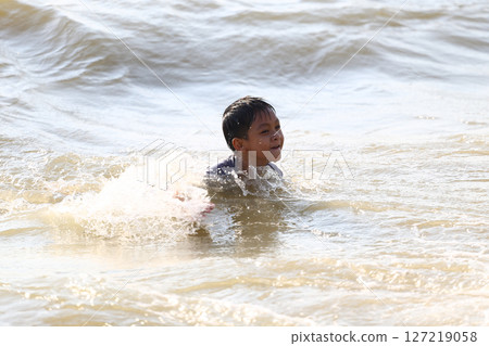 Young Boy Enjoying a Day at the Beach, Playing in the Shallow Water While Splashing and Having Fun Under the Bright Sunlight on a Summer Afternoon Young Boy Enjoying a Day at the Beach, Playing in the Shallow Water While Splashing and Having Fun Under the Bright Sunlight on a Summer Afternoon 127219058