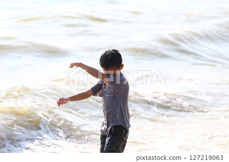 Child Playing Joyfully in Shallow Ocean Water, Splashing Waves, Sunny Day at the Beach, Summer Fun, Carefree Moments Captured in Bright Light 127219063
