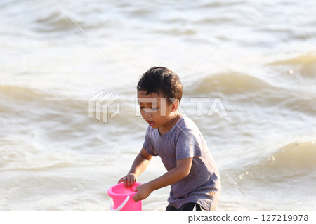 Young Boy Playing Joyfully on the Beach with Pink Bucket, Enjoying a Sunny Day by the Water, Creating Memories and Exploring Nature 127219078