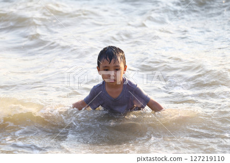 Young boy enjoying a playful moment in the shallow waves of the ocean, experiencing the joy of water play during a sunny day at the beach. 127219110