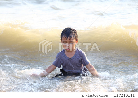 Young Boy Playing in the Shallow Water of the Ocean, Enjoying the Waves on a Sunny Day at the Beach with a Calm and Serene Expression of Bliss 127219111