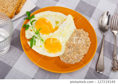 Portion of diet food on plate - two fried eggs and boiled oatmeal porridge 127219149