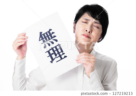 A middle-aged woman wearing a white shirt grimacing and holding a piece of paper that says "impossible" 127219213