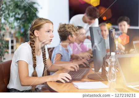 Portrait of teen schoolgirl sitting at table in computer class during lesson, smiling at camera. Concept of teenagers and technologies Portrait of teen schoolgirl sitting at table in computer class during lesson, smiling at camera. Concept of teenagers and technologies 127219231
