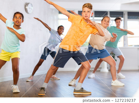 Positive juvenile boy engaged in Hip-hop dance in training room with children's group Positive juvenile boy engaged in Hip-hop dance in training room with children's group 127219237