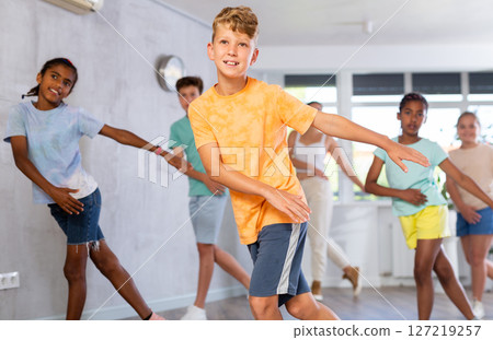 Positive juvenile boy engaged in Hip-hop dance in training room with children's group Positive juvenile boy engaged in Hip-hop dance in training room with children's group 127219257