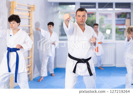 Karate instructor demonstrating kata sequence of movements to group of teenagers 127219264
