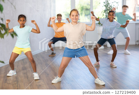 Cheerful preteen girl practicing hip-hop movements during group training Cheerful preteen girl practicing hip-hop movements during group training 127219400
