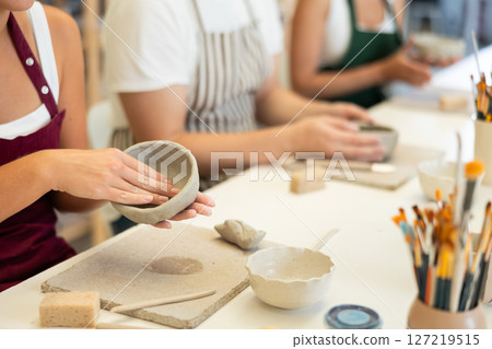 Female hands forming plate from wet clay in pottery workshop 127219515