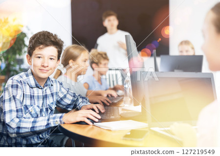 Smiling preteen boy sitting at computer table in training room Smiling preteen boy sitting at computer table in training room 127219549