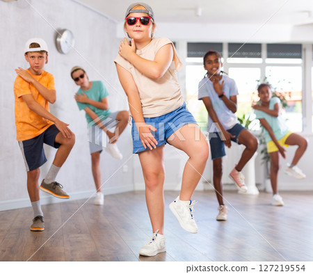 Cheerful preteen girl practicing hip-hop movements during group training Cheerful preteen girl practicing hip-hop movements during group training 127219554