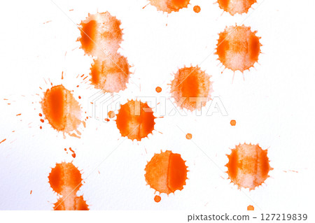 Orange color paint drops on paper, causing dispersion of color. 127219839