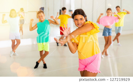 Smiling latin american preteen girl training vigorous dance with tweens 127219929