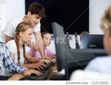 Computer science teacher helps young schoolgirl solve problem on computer 127219930