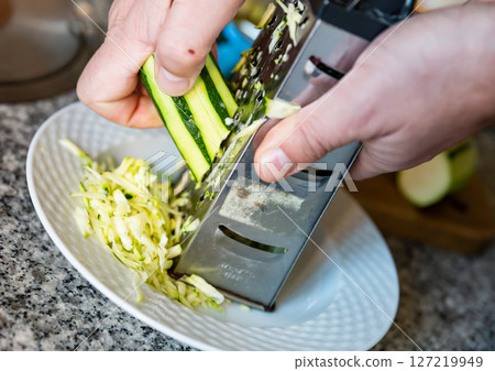 Hands rubs zucchini on grater close-up Hands rubs zucchini on grater close-up 127219949