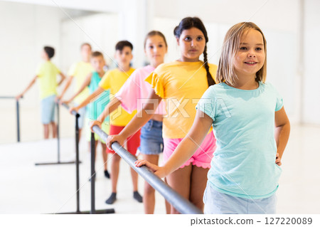 Children standing along ballet bar in dance studio during dance class 127220089