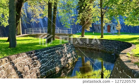 A tranquil park with a serene river, stone wall, and charming bridge A tranquil park with a serene river, stone wall, and charming bridge 127220570