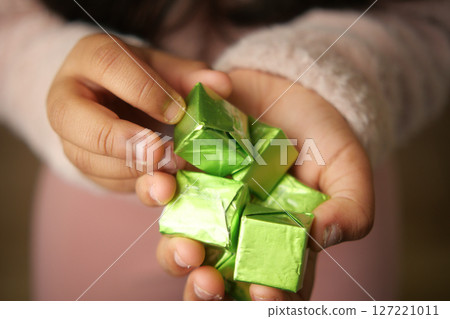 A Childs Hands Holding Colorful Green Wrapped Candies and Treats 127221011