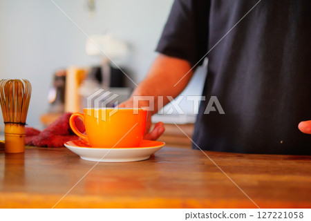 Carefully and intentionally placing a vibrant orange cup on a wooden table Carefully and intentionally placing a vibrant orange cup on a wooden table 127221058
