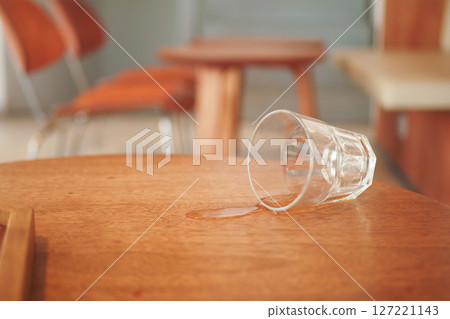 A glass has been spilled on a wooden table inside a modern cafe environment A glass has been spilled on a wooden table inside a modern cafe environment 127221143