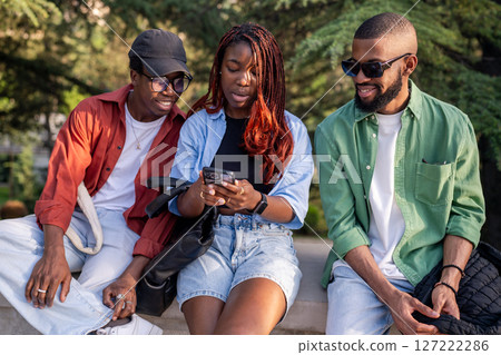 Lively African American friend sit in park, phone in hand. Woman shares trending social media post 127222286