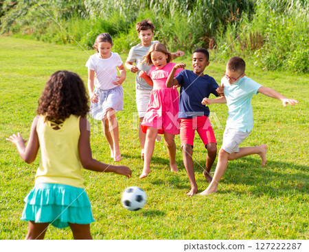 Happy preteen girls and boys playing football on green lawn 127222287