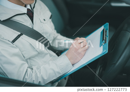 A man wearing work clothes and a tie making a rounds in a car A man wearing work clothes and a tie making a rounds in a car 127222773