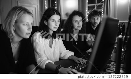 Group of young adults collaborating on computer project during evening session in cozy indoor workspace 127222829