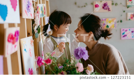 Mom and daughter enjoy colorful art creation in a cozy studio space filled with flowers and paintings 127223151