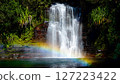 Majestic waterfall cascading into a pool with lush greenery and a vibrant rainbow displayed at the bottom 127223422