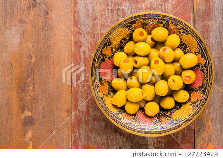 Fresh green olives are presented in an ornate bowl on weathered wooden surface. Fresh green olives are presented in an ornate bowl on weathered wooden surface. 127223429