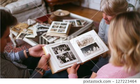 Family members share memories while looking at old photographs in a cozy living room during an afternoon gathering 127223464