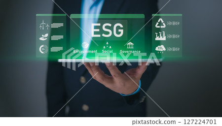Hand holding tablet displaying holographic ESG interface with Environment, Social, Governance icons. Symbolizes sustainable business, corporate responsibility, ethical investment for future impact now 127224701