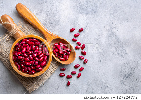Top view of raw red kidney beans in wooden bowls with a rustic sackcloth on a gray textured surface 127224772